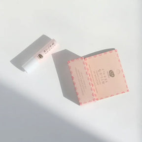 A stick of Whamisa Organic Flower Lip Balm on a white table, and its pink packaging box