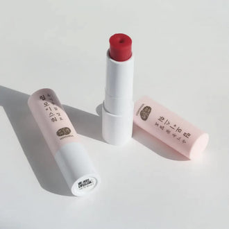 Two sticks of Whamisa Organic Flower Lip Balm on a white table, one opened and one closed