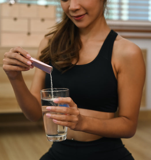 Fit girl pouring powdered supplement into a glass of water